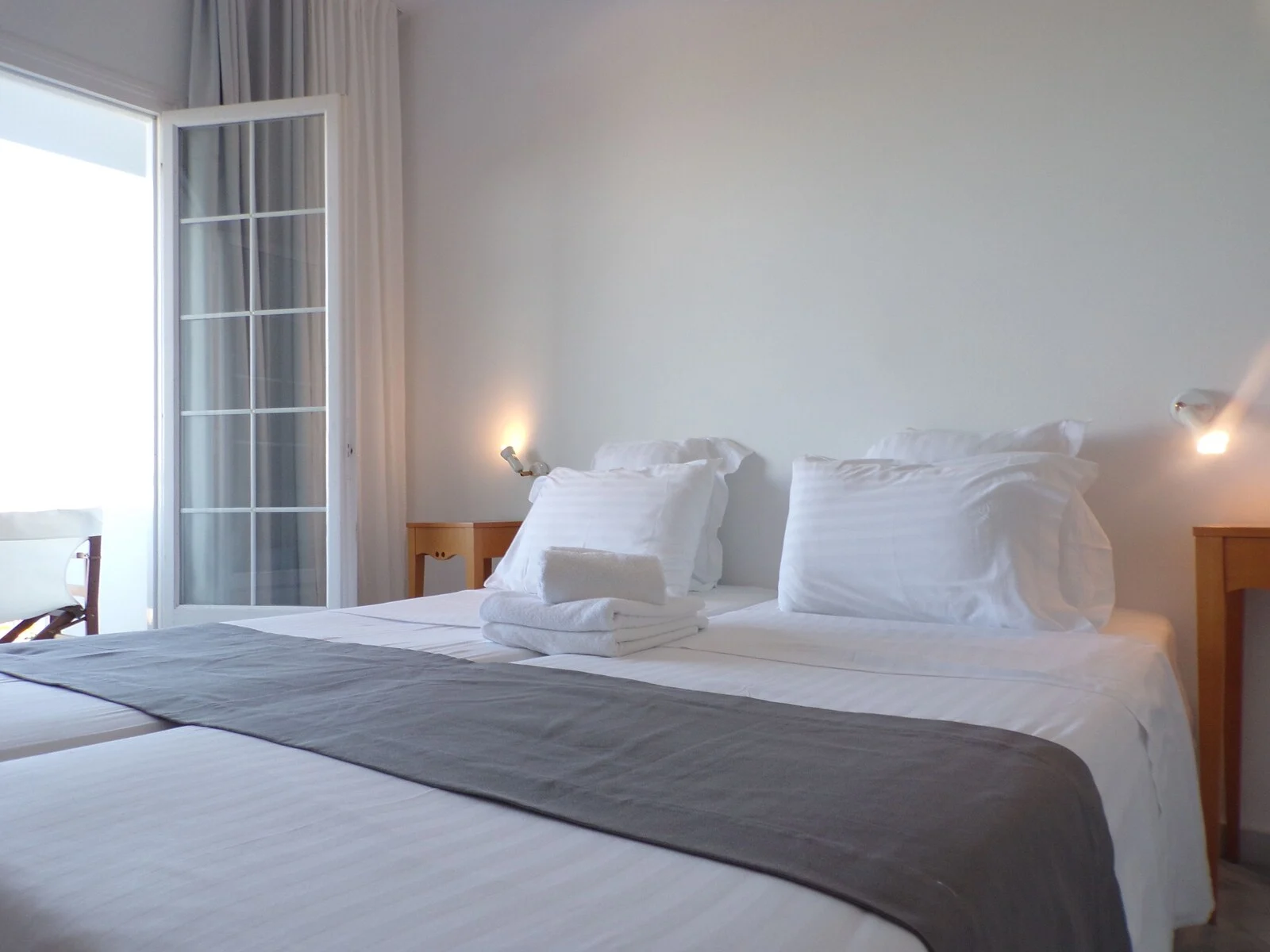 Bright bedroom with two adjacent beds and an open balcony door.