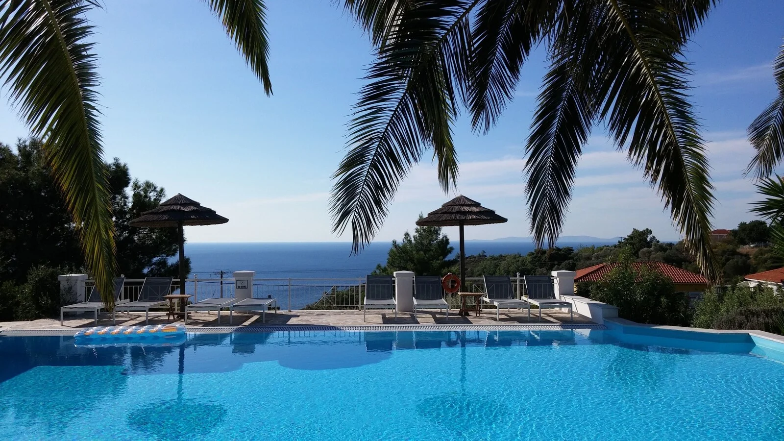 Swimming pool with loungers and parasols facing the sea.
