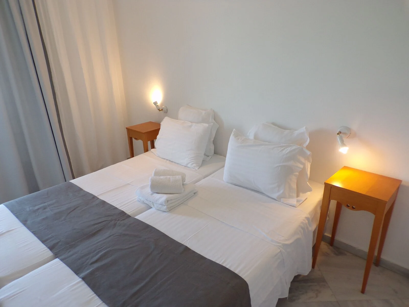 Bedroom with adjacent beds, folded towels and bedside lights.