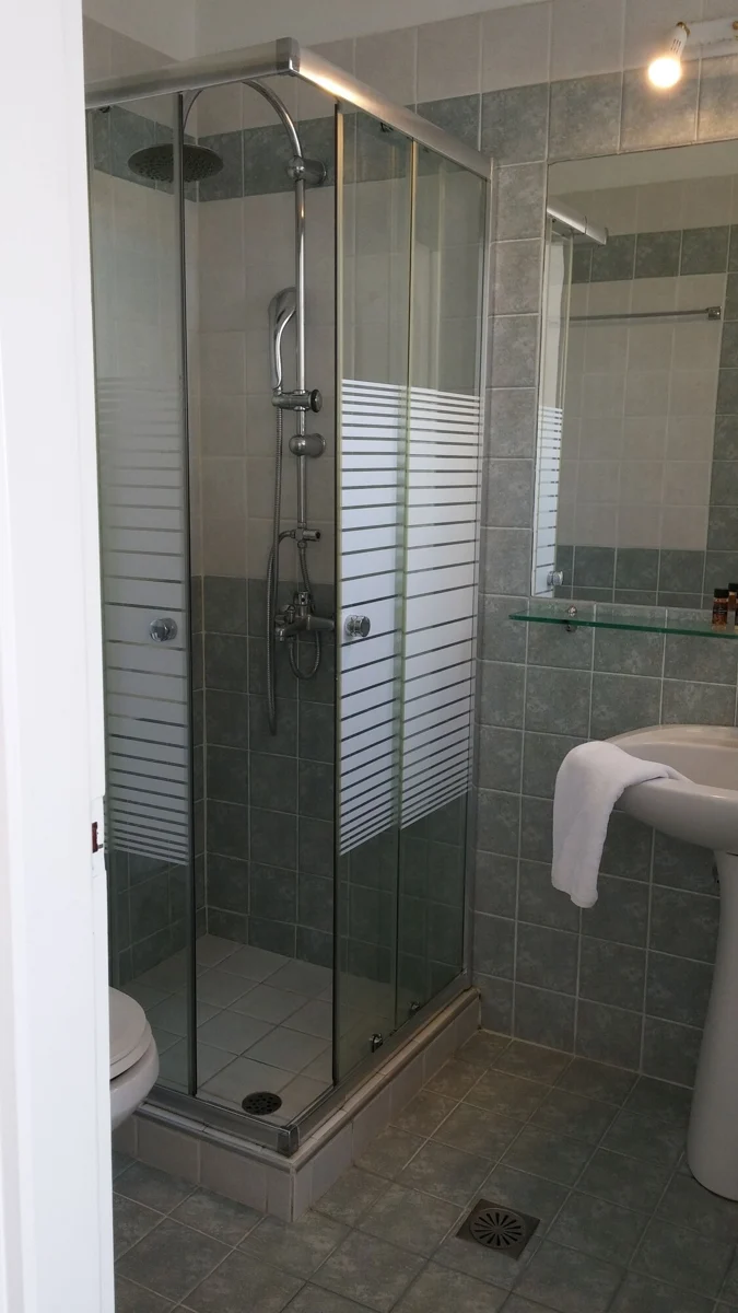 Glass shower enclosure and washbasin in a tiled bathroom.