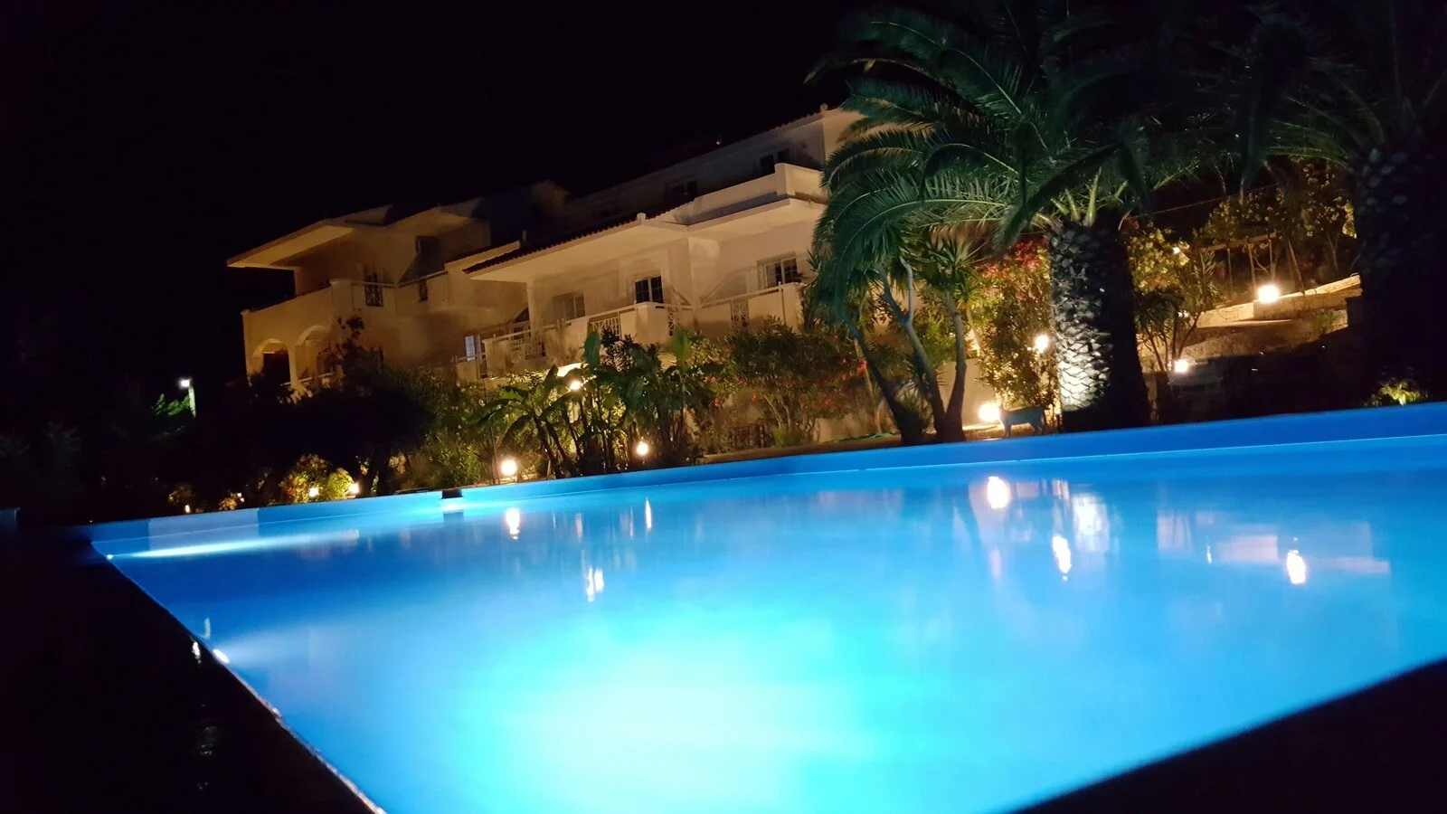 Illuminated blue pool and accommodation building at night.