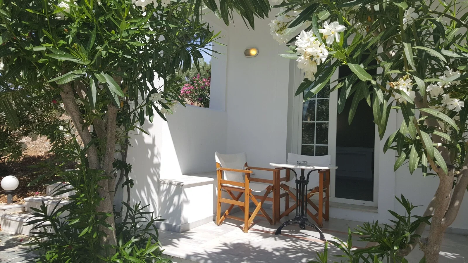 Small furnished patio beside white doors and garden plants.